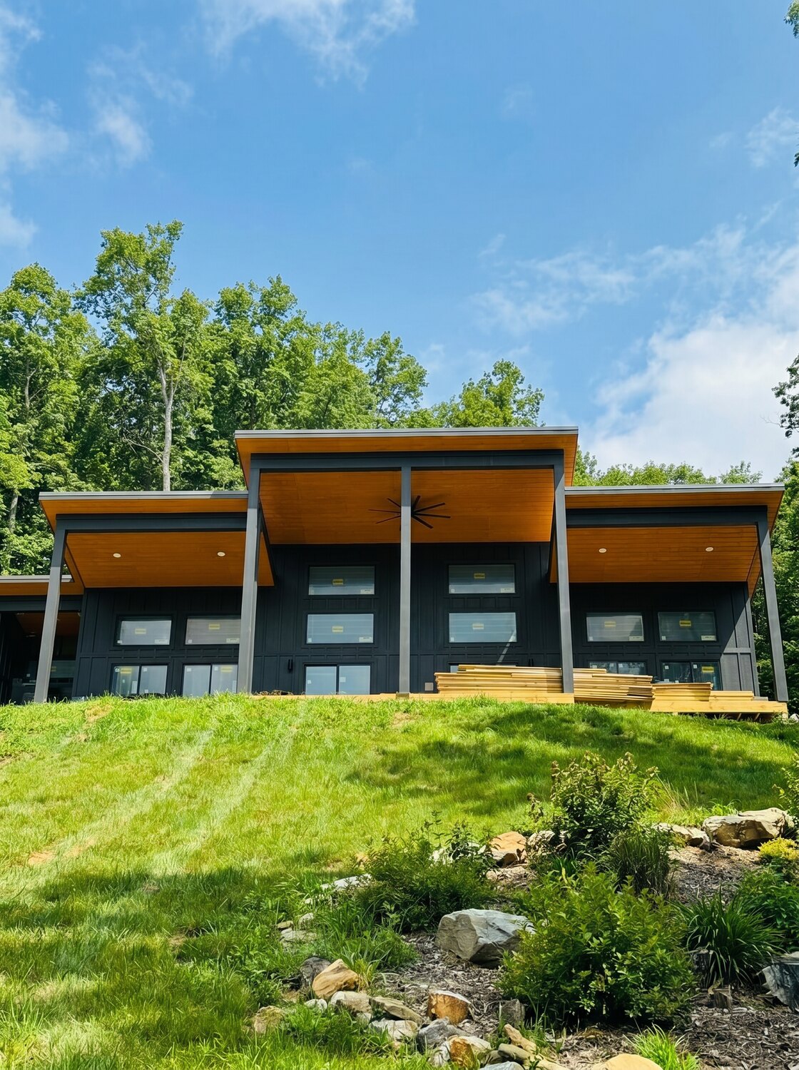 A modern Spica Homes build with a raised cedar-soffit roofline and floor-to-ceiling windows on a green summer hillside
